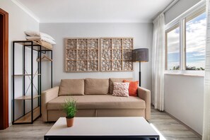 A living room with a beige sofa, a potted plant, a floor lamp, and a large window.