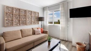 A modern living room with a sofa, a flat-screen TV, a large window with curtains, and a decorative wall panel.