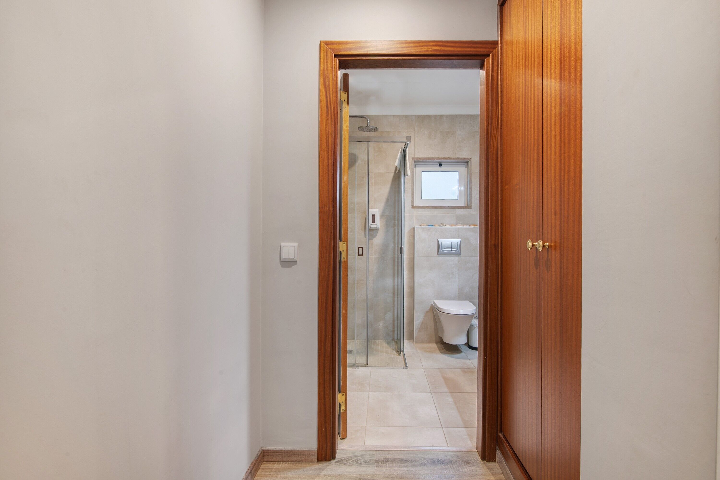 Un couloir menant à une salle de bain équipée d’une douche à parois de verre, de toilettes et d’une porte en bois.