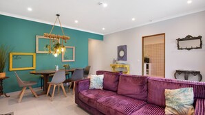 Ein Wohnzimmer mit einem violetten Sofa, einem Esstisch mit Stühlen, einer Kandelaber und gerahmten Bildern an der Wand.