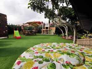 A backyard with artificial grass, a climbing wall, a slide, and a patio area with a table and chairs.