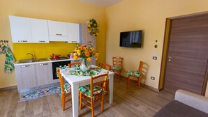 A compact kitchen with white cabinets, a dining table with chairs, a TV mounted on the wall, and a wooden door. - Holiday Home 'Ficurigna' with Private Garden, Wi-Fi and Air Conditioning (Marsala)