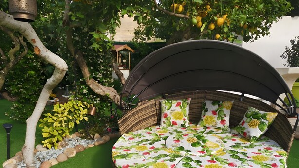 A round wicker outdoor seating area with a canopy, surrounded by a garden with artificial grass, rocks, and plants. - Holiday Home 'Ficurigna' with Private Garden, Wi-Fi and Air Conditioning (Marsala)