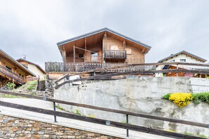 A wooden chalet with a balcony, a stone retaining wall, and a concrete staircase.