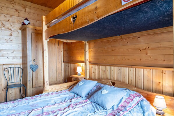 Une pièce de cabane en bois comprenant un lit, une chaise, une table de chevet et une décoration en forme de cœur accrochée au mur.