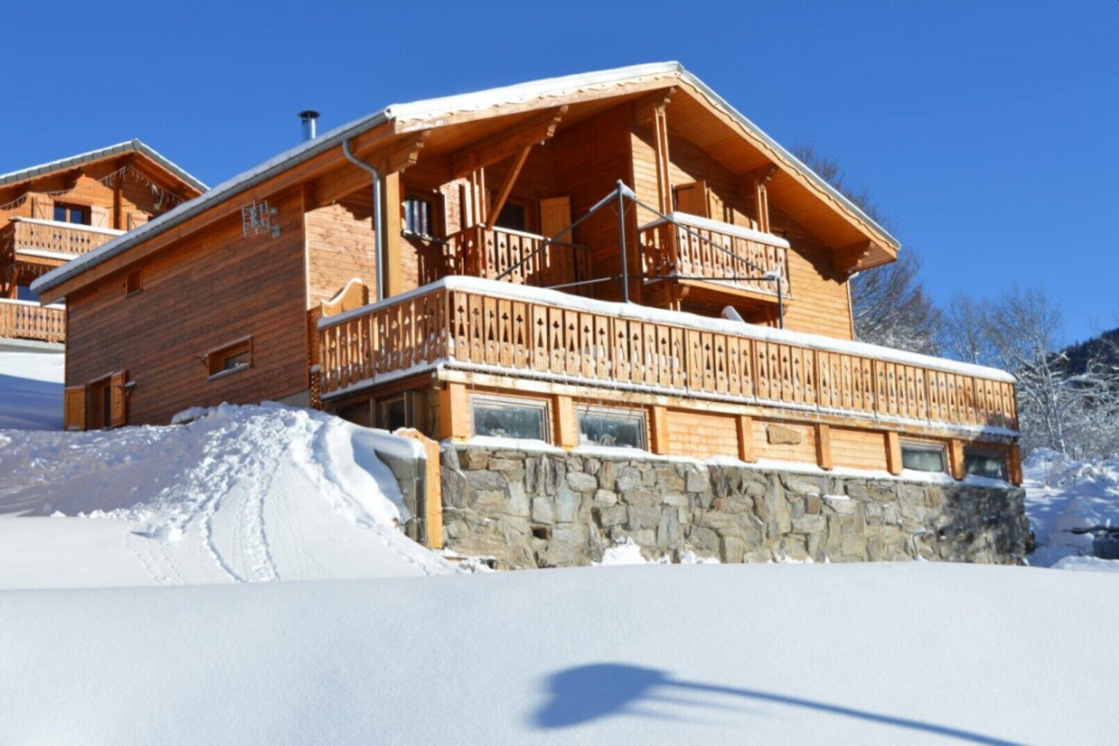 Een houten chalet met balkon, stenen fundering en een besneeerd landschap.