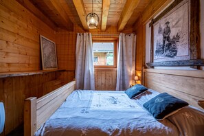 Une pièce de cabane en bois comprenant un lit, des rideaux, un tableau encadré et une fenêtre.