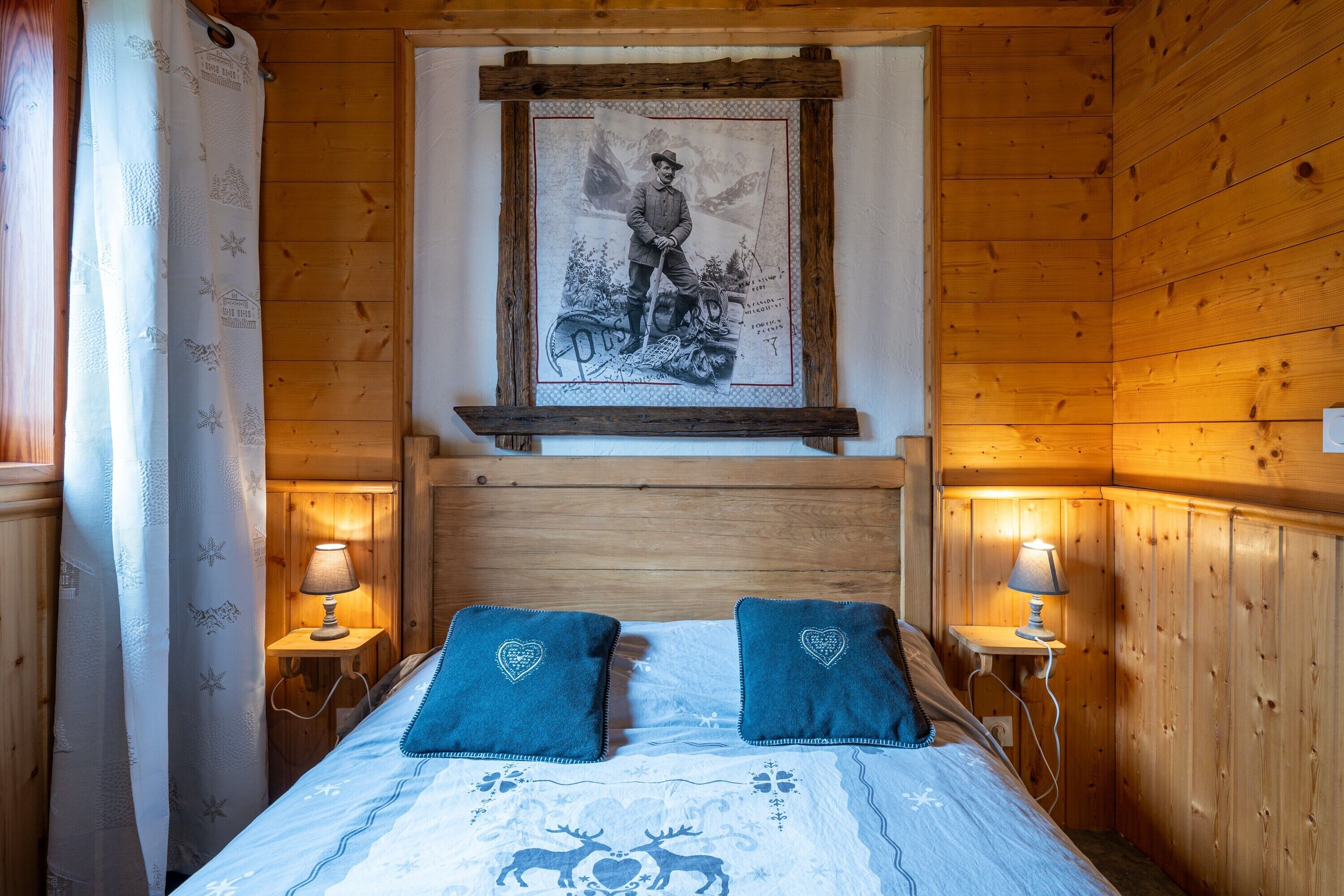 Ein Zimmer in einer Holzhütte mit einem Bett, zwei herzförmigen Kissen, einem gerahmten Bild an der Wand und zwei Nachttischlampen.