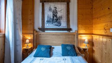 Ein Zimmer in einer Holzhütte mit einem Bett, zwei herzförmigen Kissen, einem gerahmten Bild an der Wand und zwei Nachttischlampen.