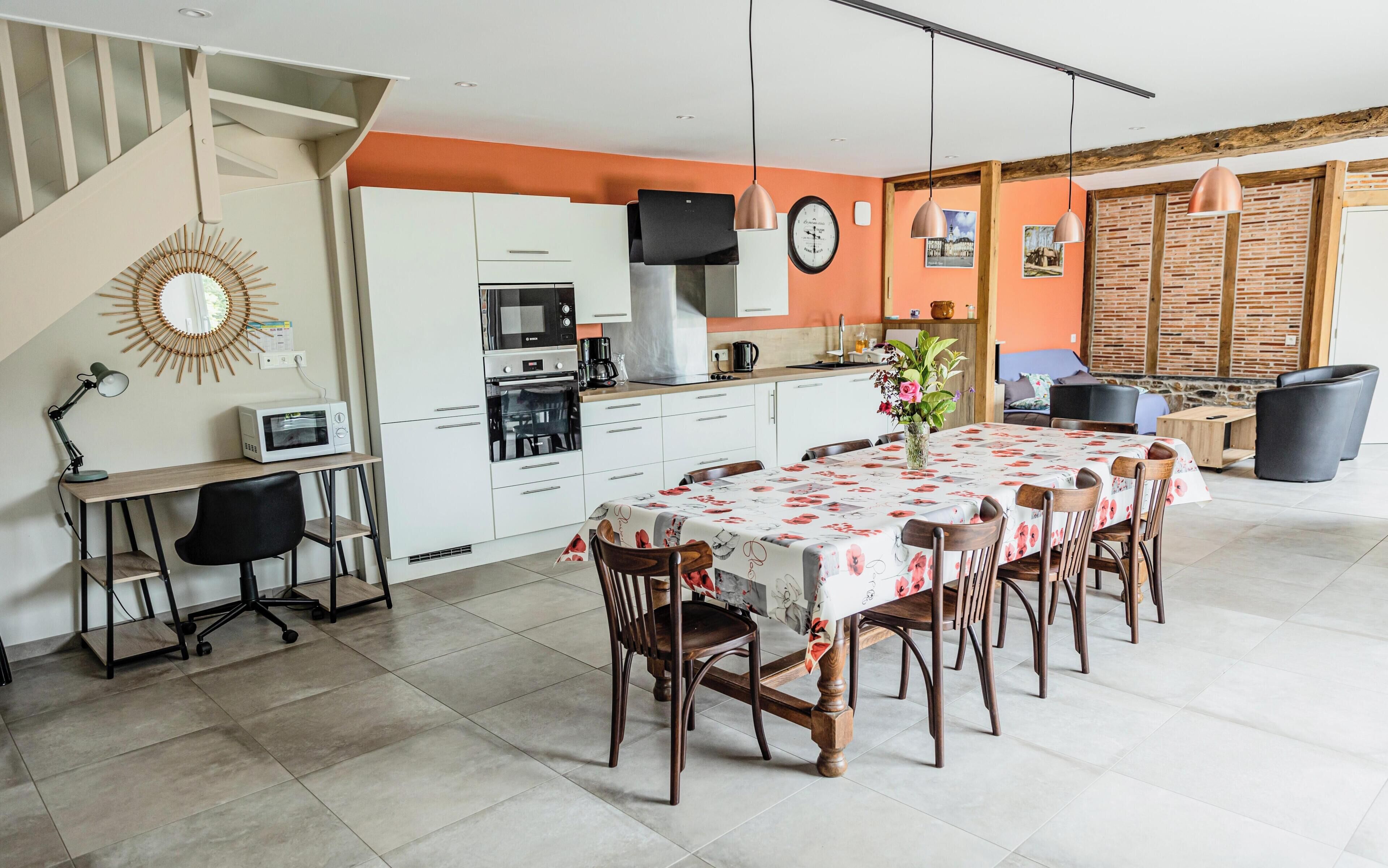 A modern kitchen with white cabinets, a dining area with a floral tablecloth, and a staircase.