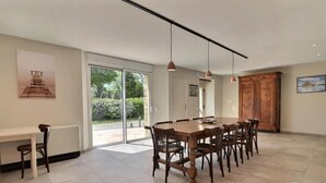 Un comedor moderno con una mesa grande, sillas, lámparas colgantes y vistas a un jardín exterior a través de puertas de cristal.