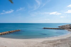 Une plage avec une eau d’un bleu limpide, une digue rocheuse et une rive sablonneuse.