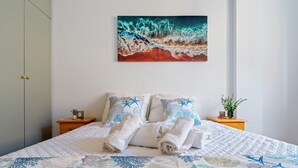 Una cama bien hecha con una colcha de estampado coralino, un cuadro de un arrecife de coral en la pared y una pequeña planta en la mesita de noche.