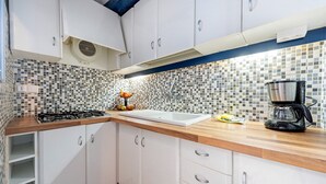 Una cocina con alacenas blancas, salpicadero de azulejos, encimera de madera, estufa a gas, lavamanos y cafetera.