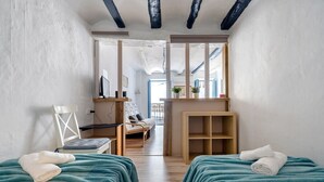 Una habitación con dos camas, un escritorio, una silla, un espejo y vista a otra habitación.