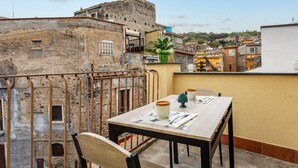 Een balkon met een tafel voor twee, met uitzicht op een historisch stadsgezicht met stenen gebouwen en een fortachtige constructie.