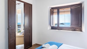 A bedroom with a bed, a window with a view of the sea, and a door leading to a balcony.