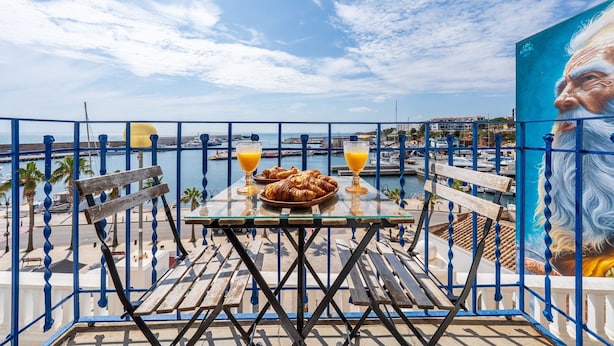 A balcony with a table, chairs, a plate of croissants, and two glasses of orange juice.