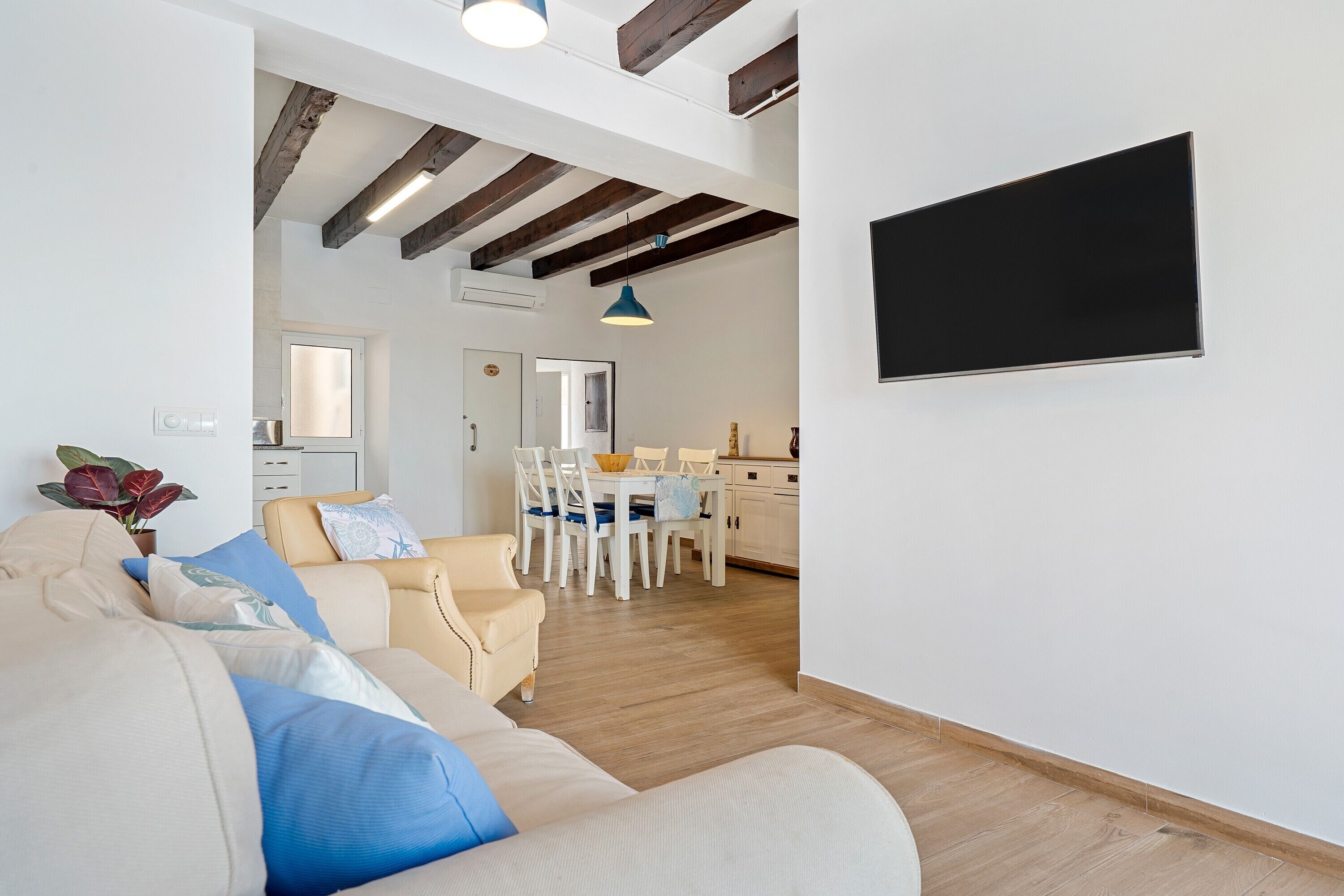 Una sala de estar con un sofá, un comedor con sillas y una mesa, y una cocina al fondo.