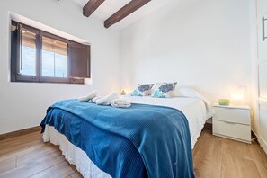 A bedroom with a bed, a nightstand, a window with blinds, and a wooden floor.
