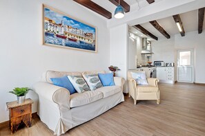 A living room with a sofa, armchair, and a painting of a coastal scene.