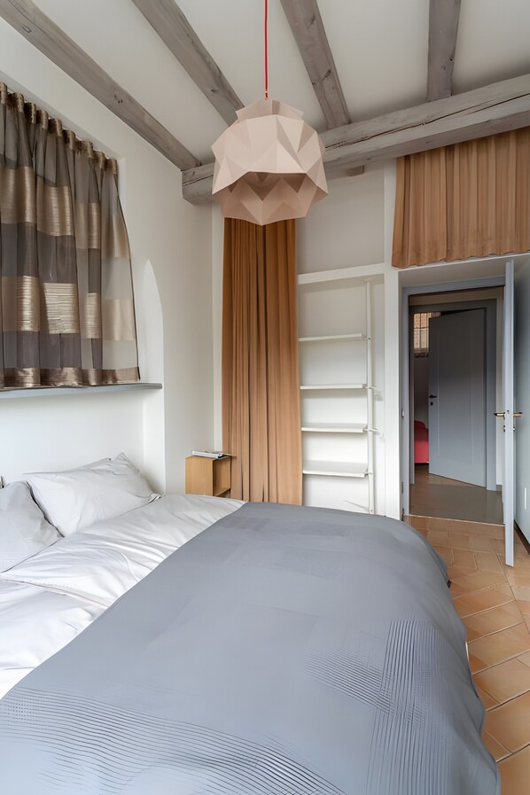 Una camera da letto con un letto, una lampada a sospensione, una finestra con tende e una porta che conduce a un'altra stanza.