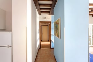 A narrow hallway with a tiled floor, a white refrigerator on the left, and a door at the end.