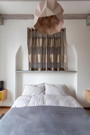 A bedroom with a bed, a geometric pendant light, and a window with striped curtains.
