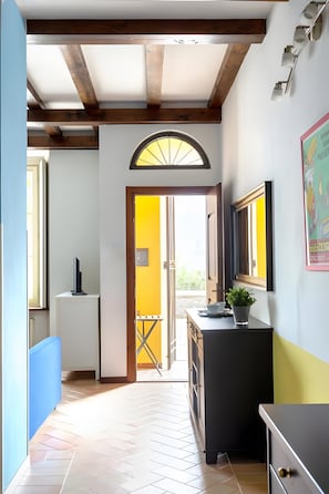 A hallway with a tiled floor, a door leading outside, a small table with a plant, and a wall-mounted light fixture.