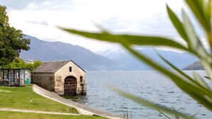 A lakeside building with a stone facade, a small adjacent structure, and a clear view of mountains in the background. - Apartment 'Vista Lago 2' with Lake View, Shared Terrace and Wi-Fi (Cannobio)