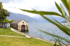Un bâtiment situé au bord du lac, doté d’une façade en pierre, d’une petite construction adjacente et offrant une vue dégagée sur les montagnes en arrière-plan.