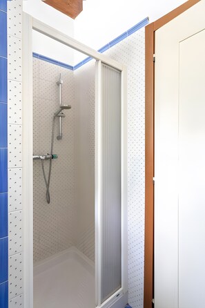 A shower with a glass door, a white tiled wall, and a blue accent wall.