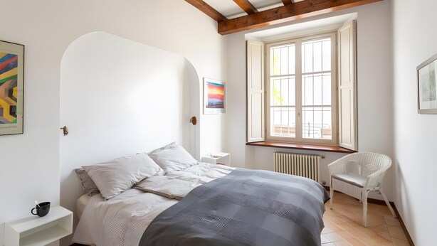 A bedroom with a bed, a chair, a window, and artwork on the walls. - Apartment 'Vista Lago 2' with Lake View, Shared Terrace and Wi-Fi (Cannobio)