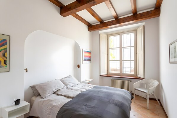 A bedroom with a bed, a chair, a window, and artwork on the walls.