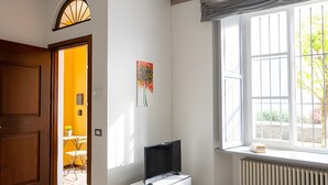 A room with a wooden ceiling, a radiator, a window with blinds, a green table, and a door leading to another room. - Apartment 'Vista Lago 2' with Lake View, Shared Terrace and Wi-Fi (Cannobio)