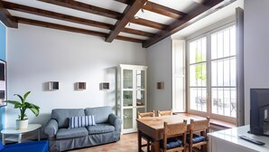 A living room with a grey sofa, wooden dining table, and chairs, a white cabinet, and a TV on a white stand. - Apartment 'Vista Lago 2' with Lake View, Shared Terrace and Wi-Fi (Cannobio)