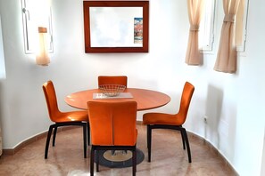 Ein Essbereich mit einem runden Tisch, vier orangefarbenen Stühlen, einem kleinen Drahtkorb und einem gerahmten Bild an der Wand.