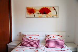 Ein Schlafzimmer mit weißem Kopfteil, zwei Nachttischen und einem Bett mit rot-weißer Karomattratzenauflage.