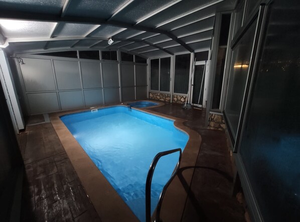 Una piscina con suelo de baldosas, una silla y un muro de piedra.
