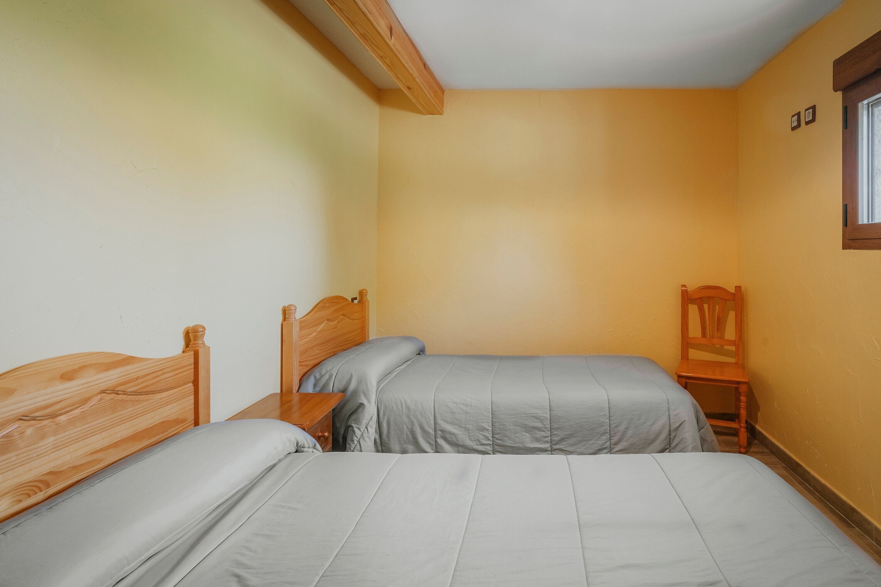 Une chambre avec deux lits, des têtes de lit en bois, une table de chevet, une chaise et une fenêtre.