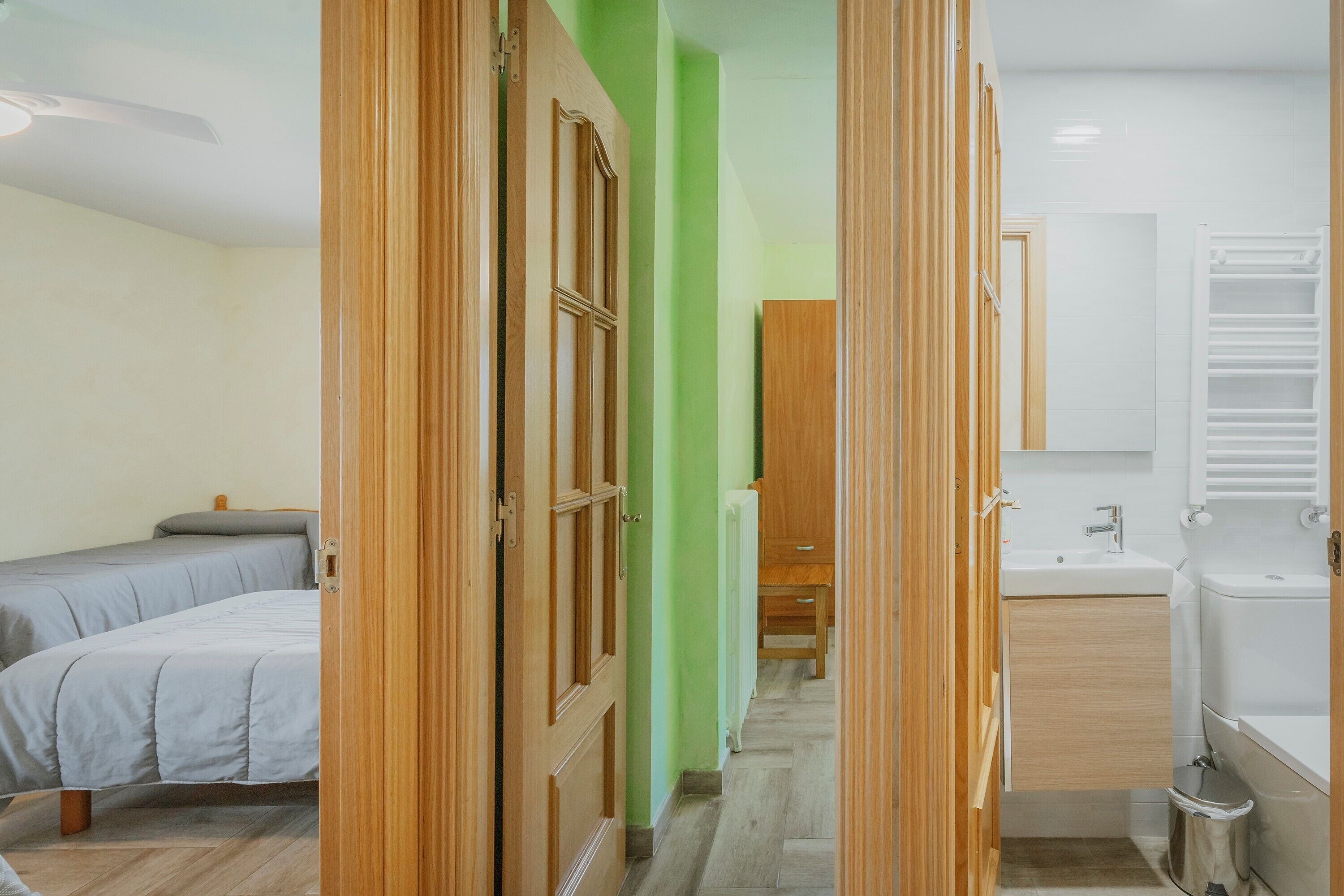 A hotel room with a bed, a bathroom with a sink and mirror, and a hallway leading to another room.