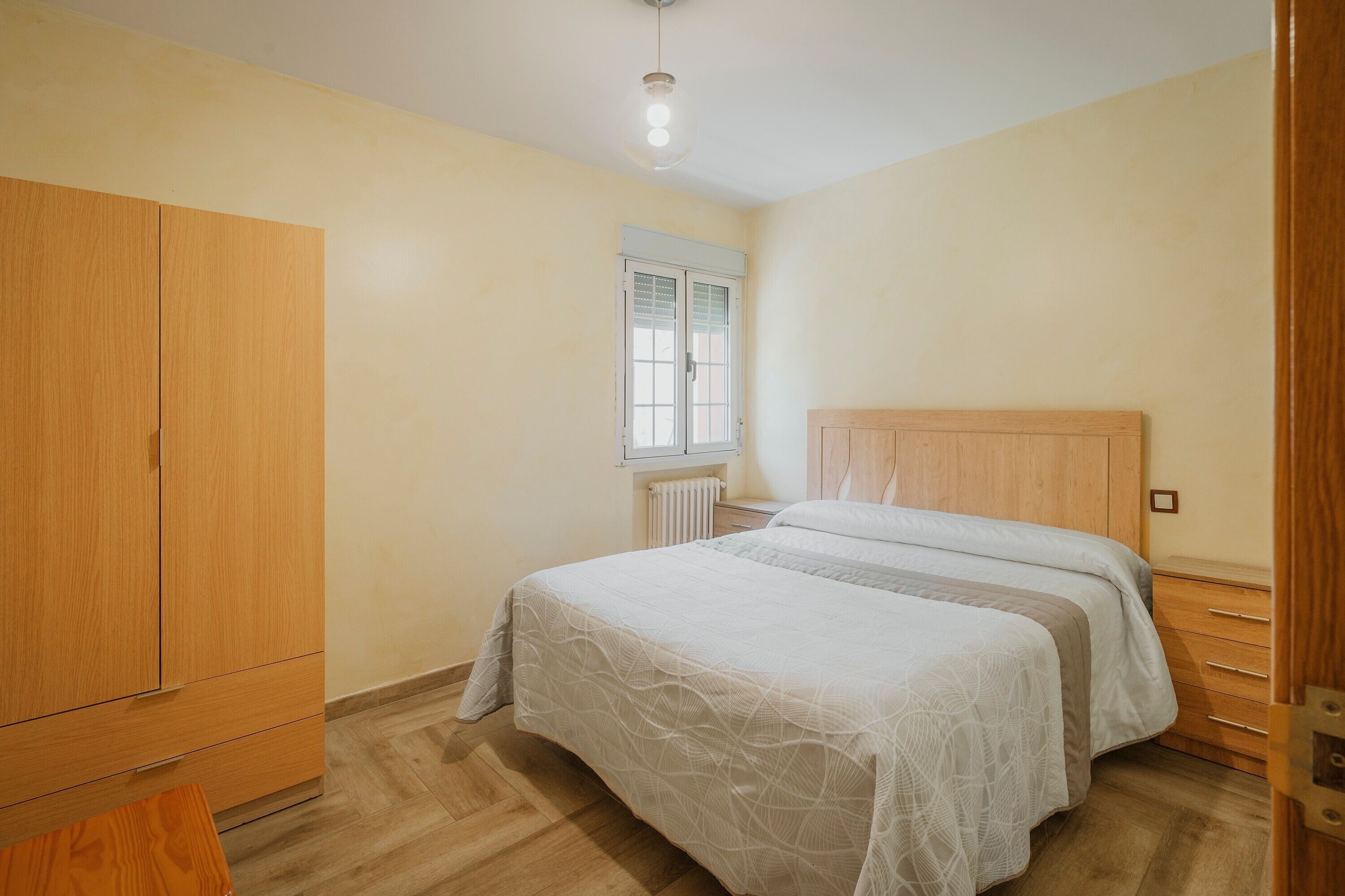 Un dormitorio con cama, armario de madera y ventana con persianas.
