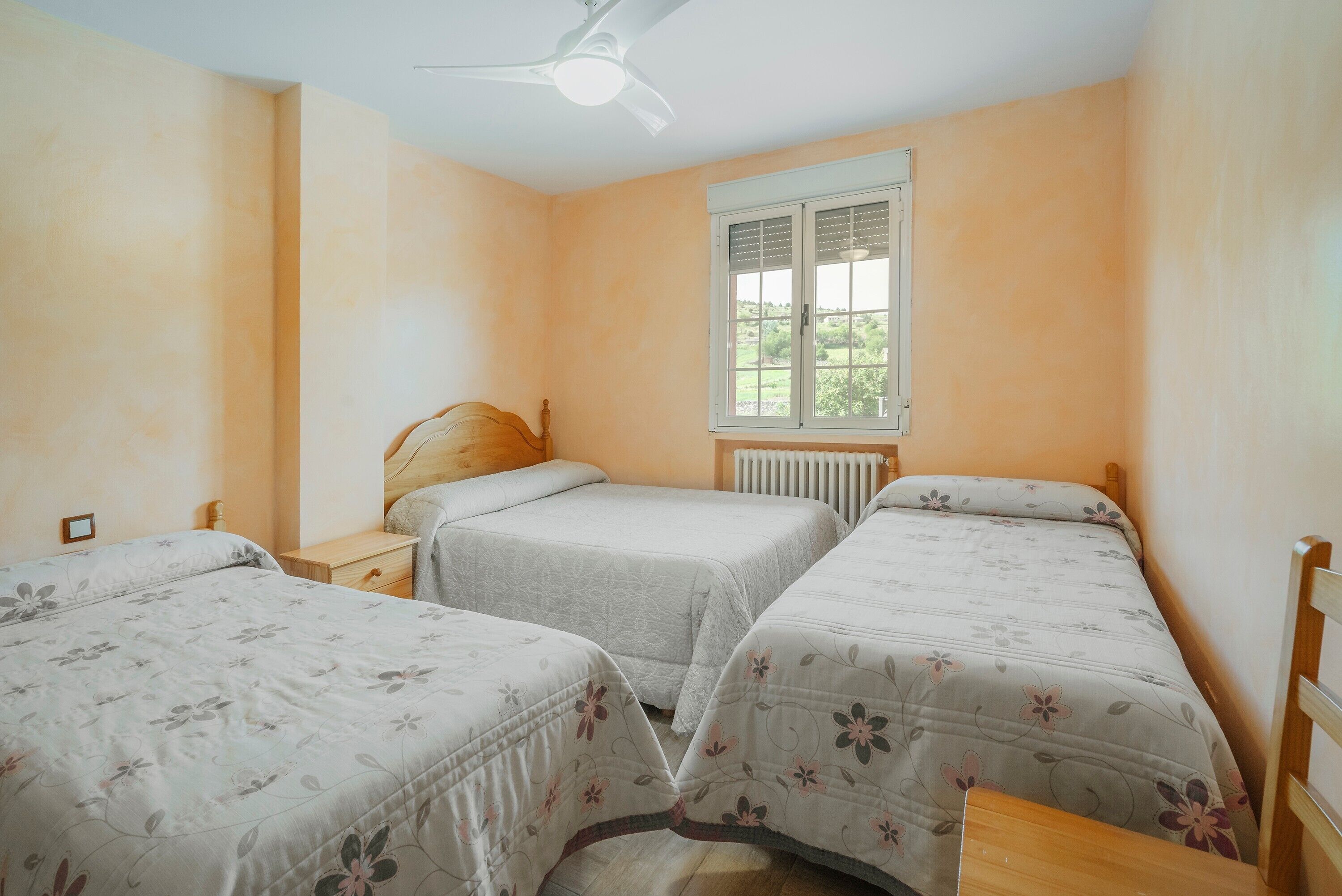 Un dormitorio con dos camas individuales, una ventana con persianas, un ventilador de techo y un radiador.