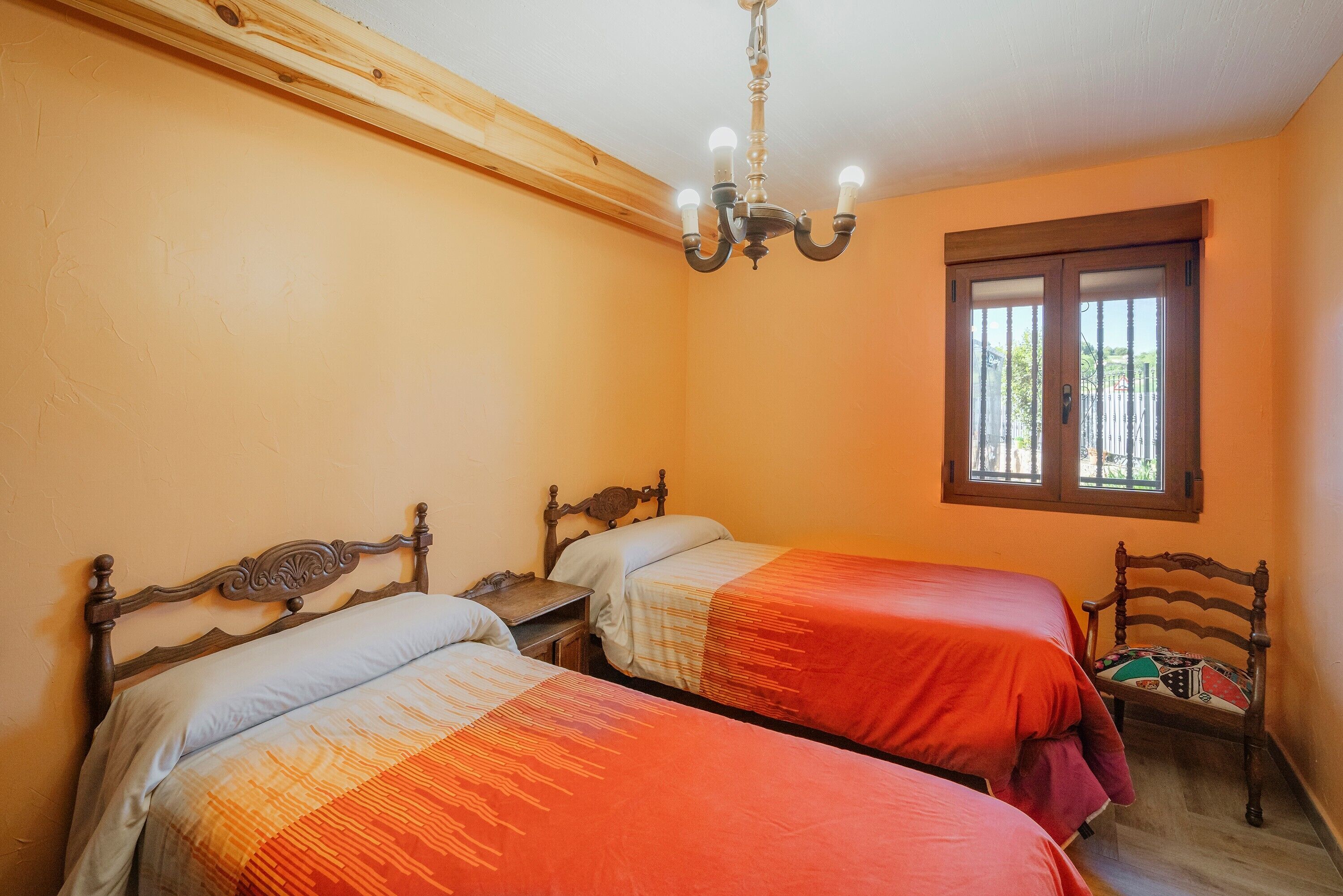 Una habitación con dos camas, cabecera de madera, ventana con persianas y una araña.