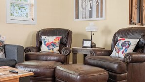 Een woonkamer met twee bruine leren fauteuils, een klein houten tafeltje en een lamp.
