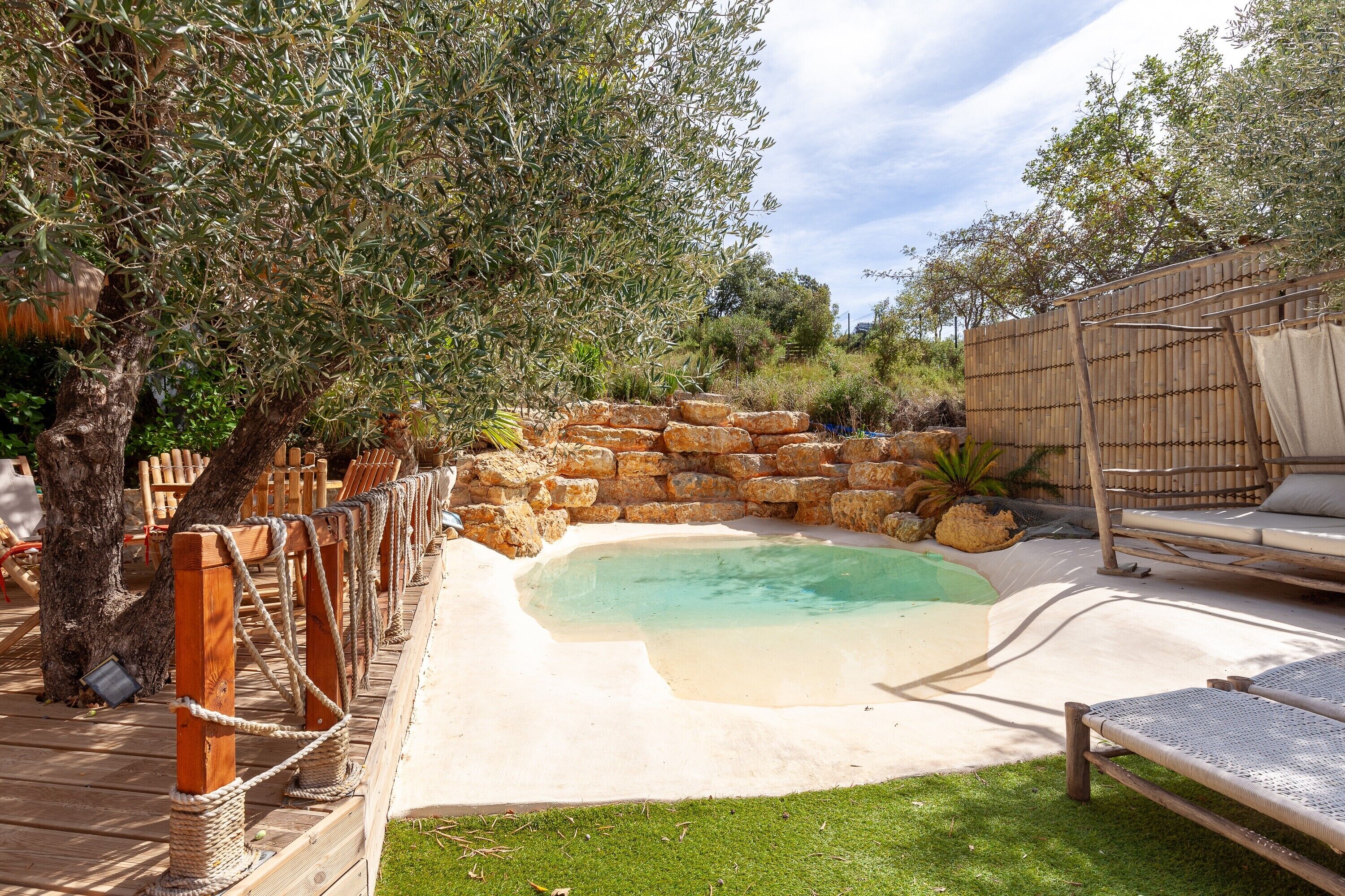 A pool area with a wooden deck, a stone wall, and a lounge chair.