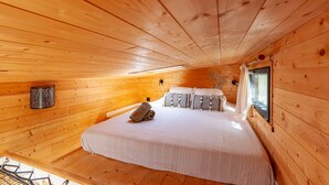 Une chambre dans une cabane en bois, avec un lit, des oreillers, une fenêtre et une lampe fixée au mur.