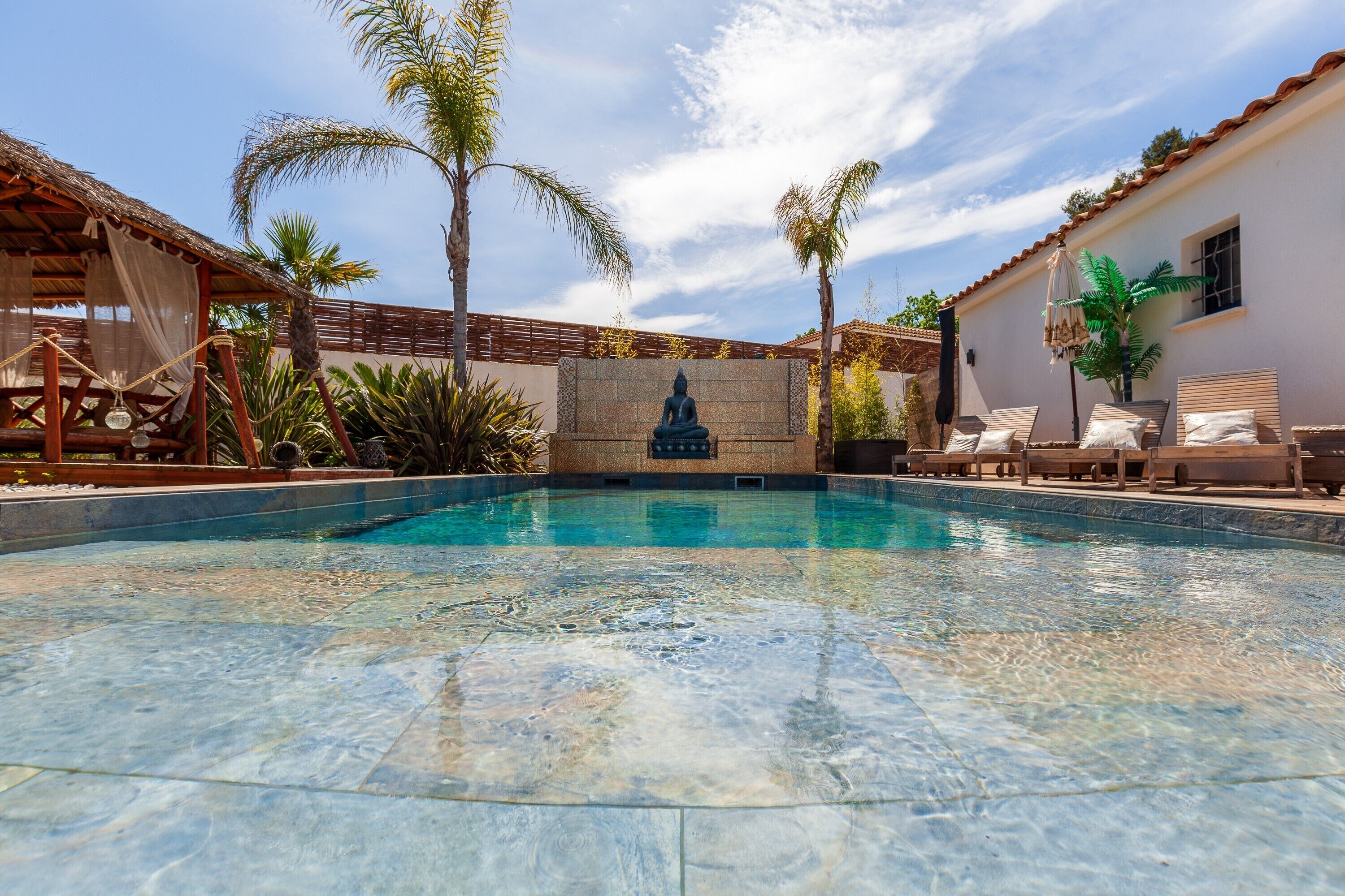 A swimming pool with a Buddha statue, palm trees, and lounge chairs.