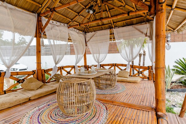 Un espace extérieur aménagé avec des meubles en osier, un toit de chaume et une vue sur la plage.