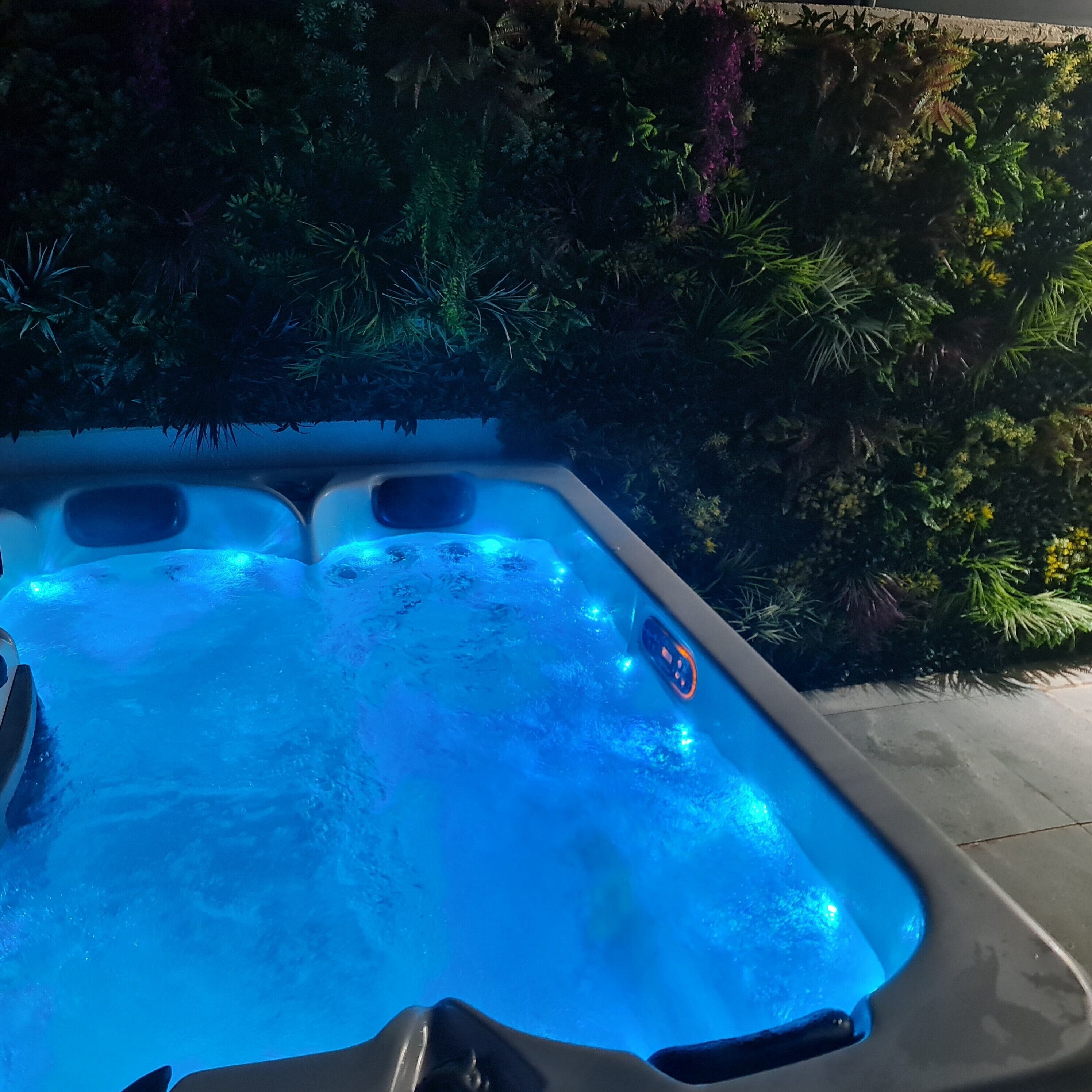 A hot tub with a control panel, surrounded by lush greenery.